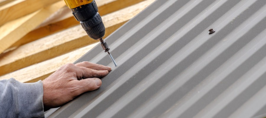 Man fastening screw to metal roof panel on building 