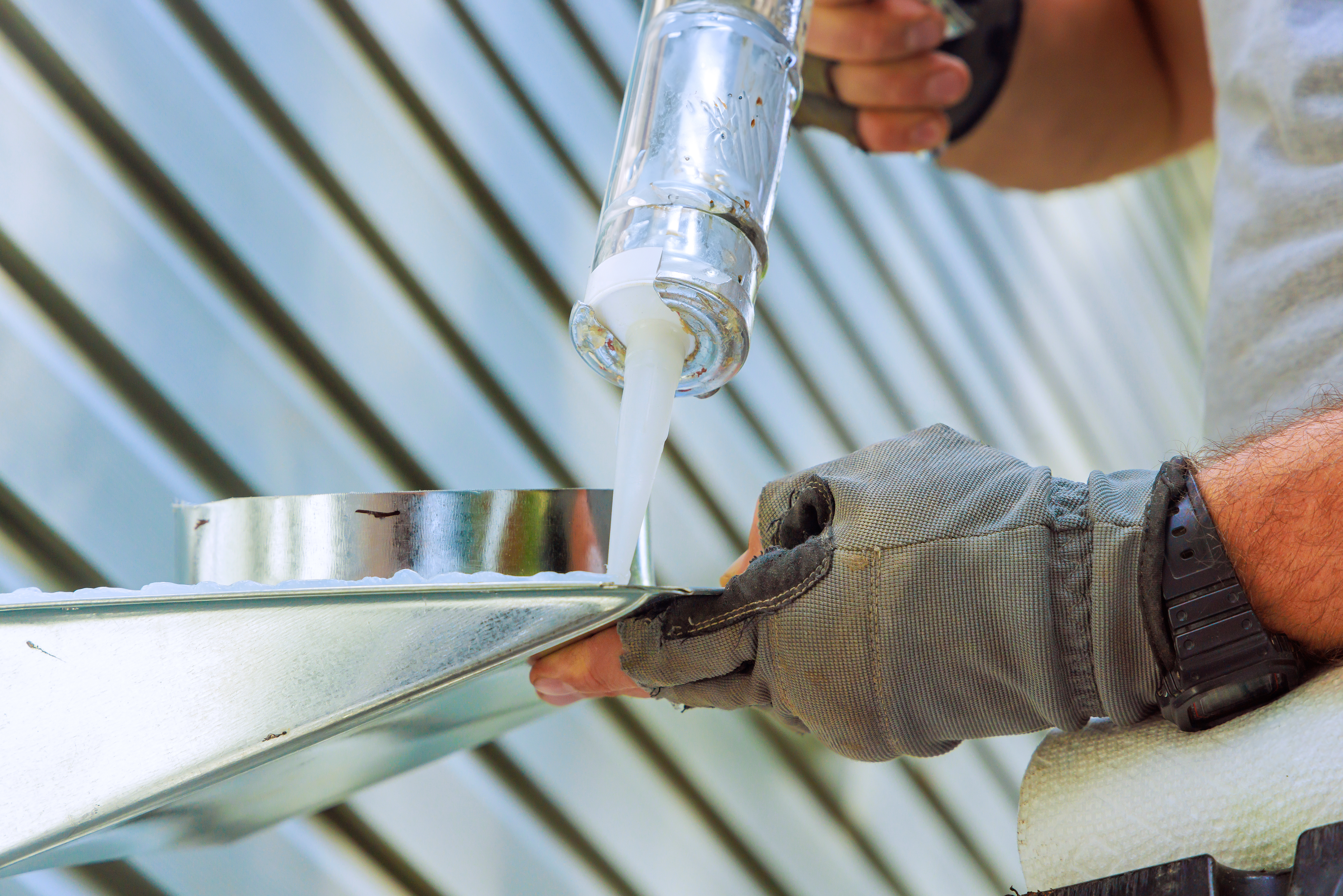 Contractor applying metal roof sealants to a metal roof.